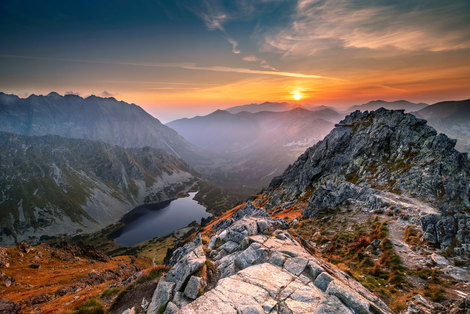 Zachód słońca nad skalistym grzbietem górskim, jezioro w dolinie