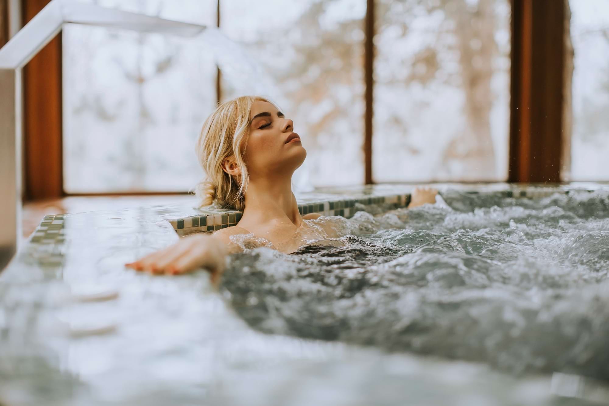 Blond kobieta relaksuje w gorącej kąpieli, zimowy widok za oknem
