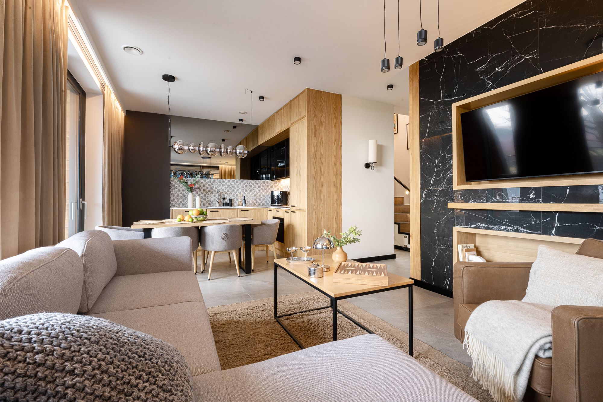 Duży salon z kuchnią, beżowa sofa, czarna marmurowa ściana i TV