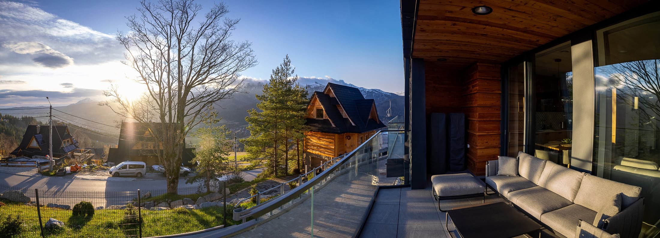 Panoramiczny widok z tarasu na górskie chaty, drzewa i słońce